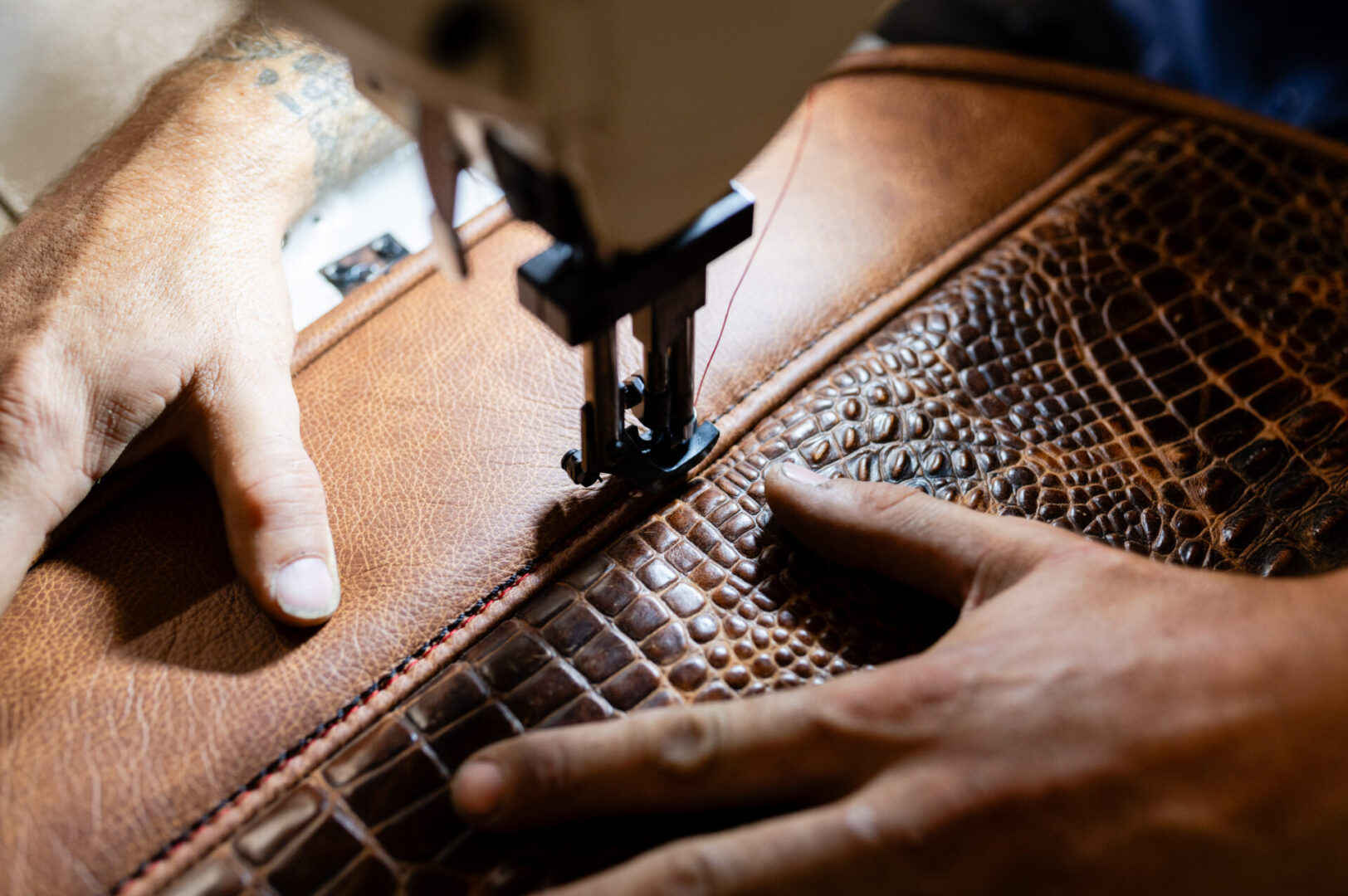 A person is sewing on a leather bag.